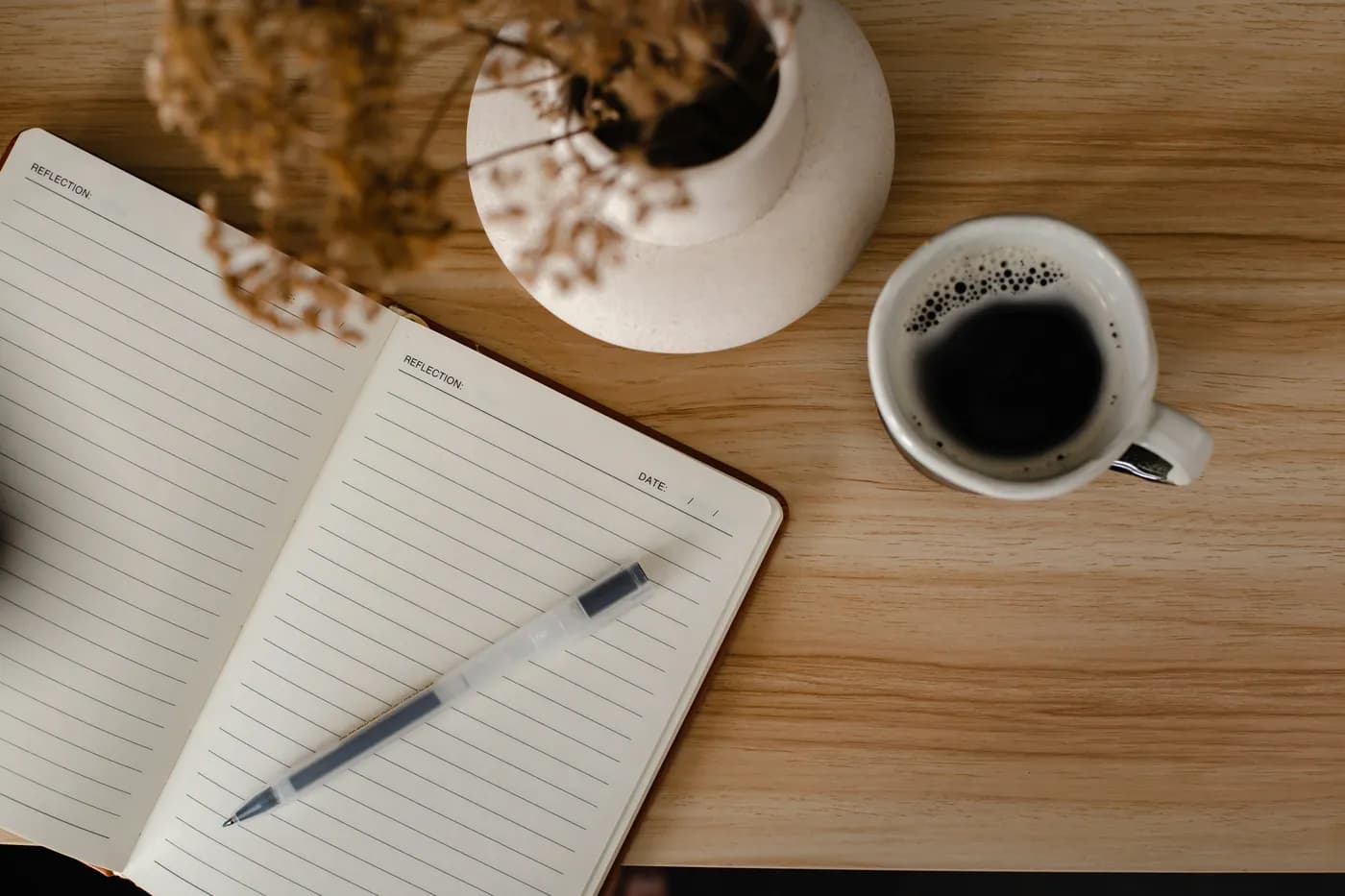 An open notebook and pen beside a cup of coffee on a wooden desk, from above