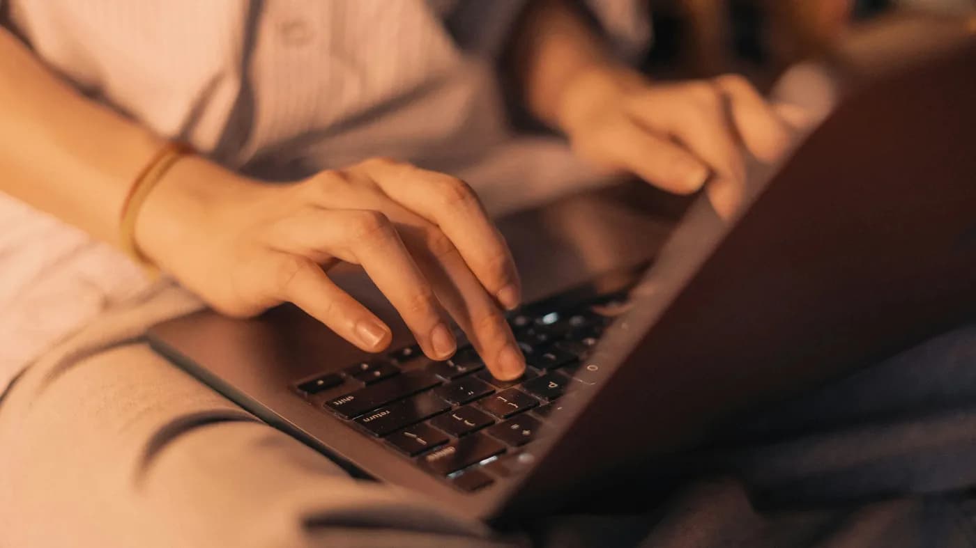 Close-up of hands typing on a laptop keyboard in warm daylight